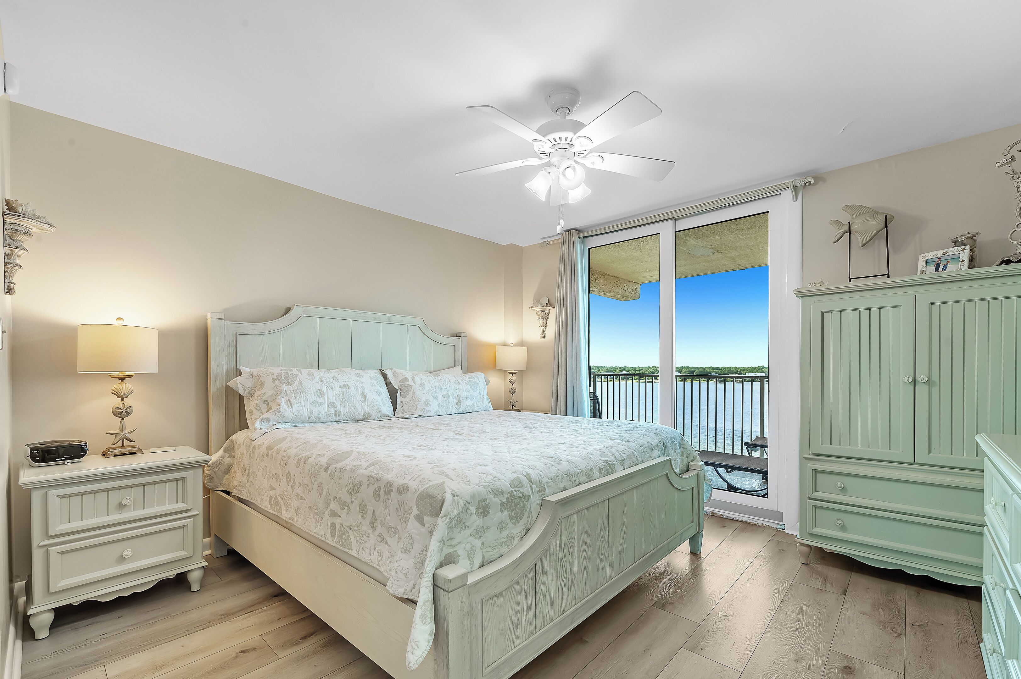 Un dormitorio con cama, mesitas de noche, ventilador de techo y vistas al exterior.