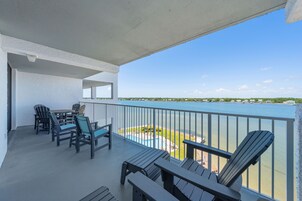 A balcony with chairs and a table, overlooking a body of water and a distant shoreline.