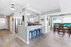 A modern kitchen with white cabinets, a stainless steel refrigerator, and a bar area with blue stools.