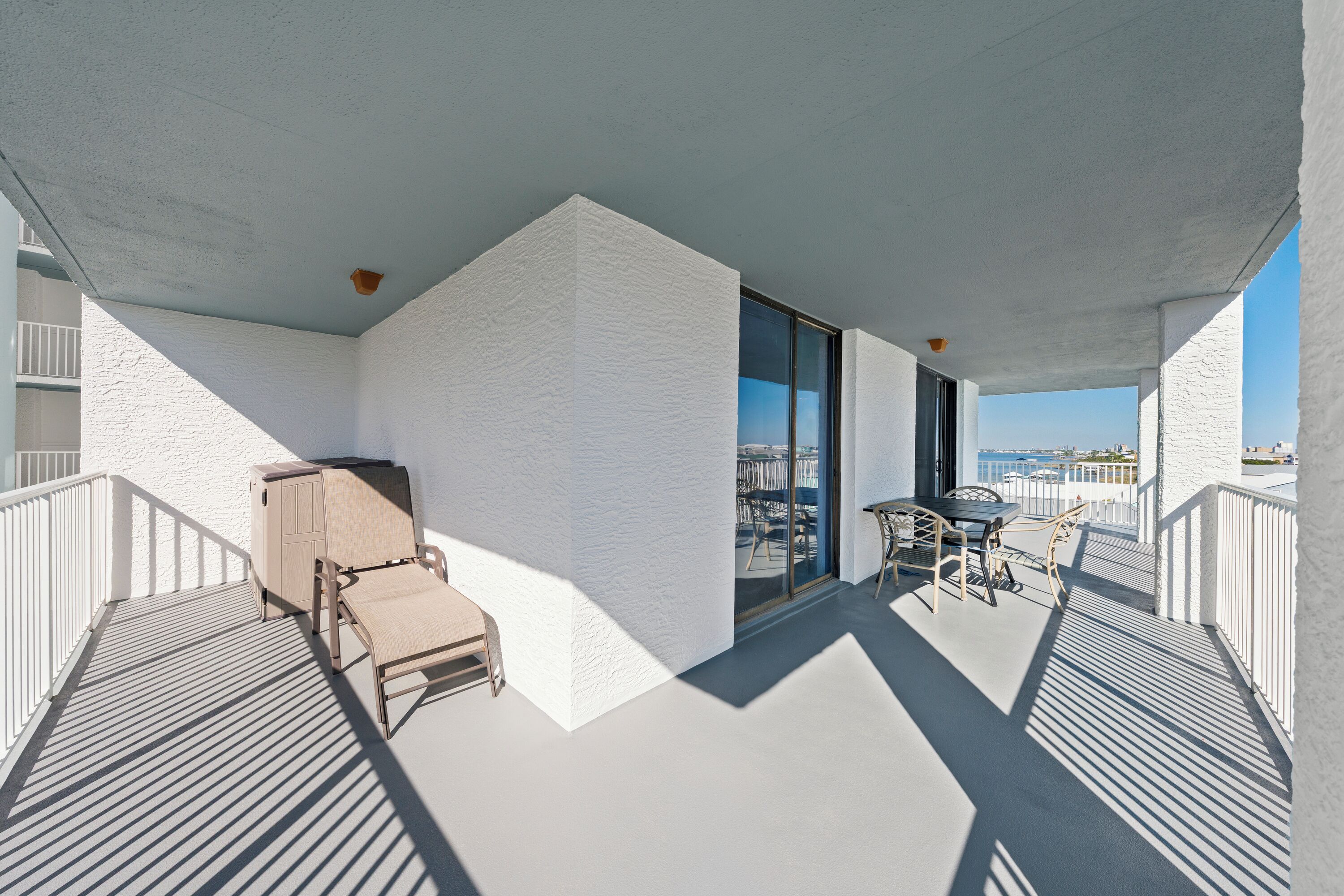 A balcony with a white textured wall, a wooden cabinet, a chair, and a table with chairs.