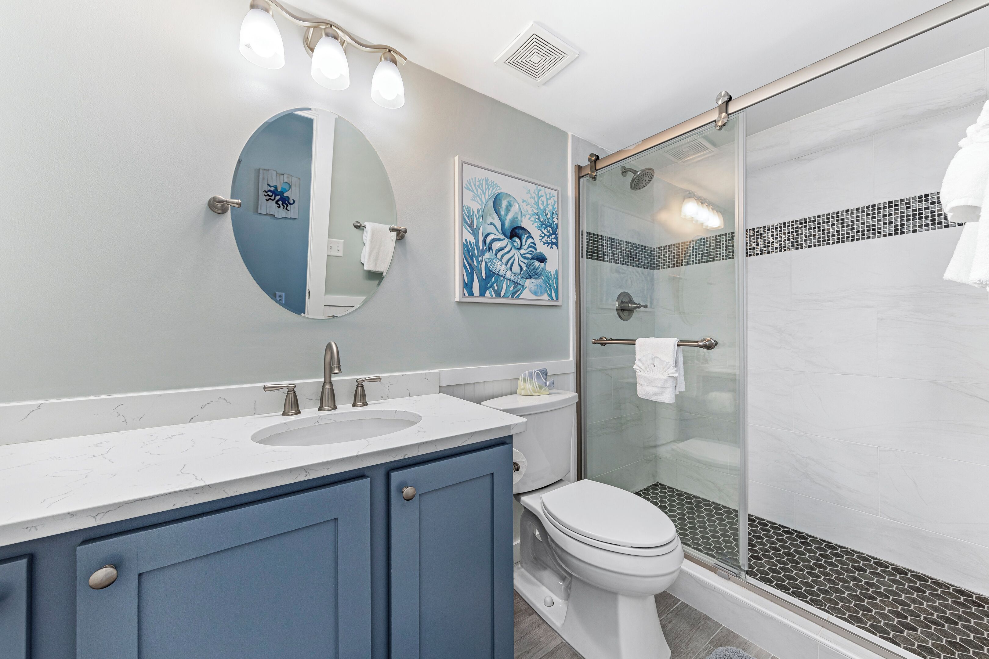 A modern bathroom with a glass-enclosed shower, a sink with a marble countertop, and a toilet.