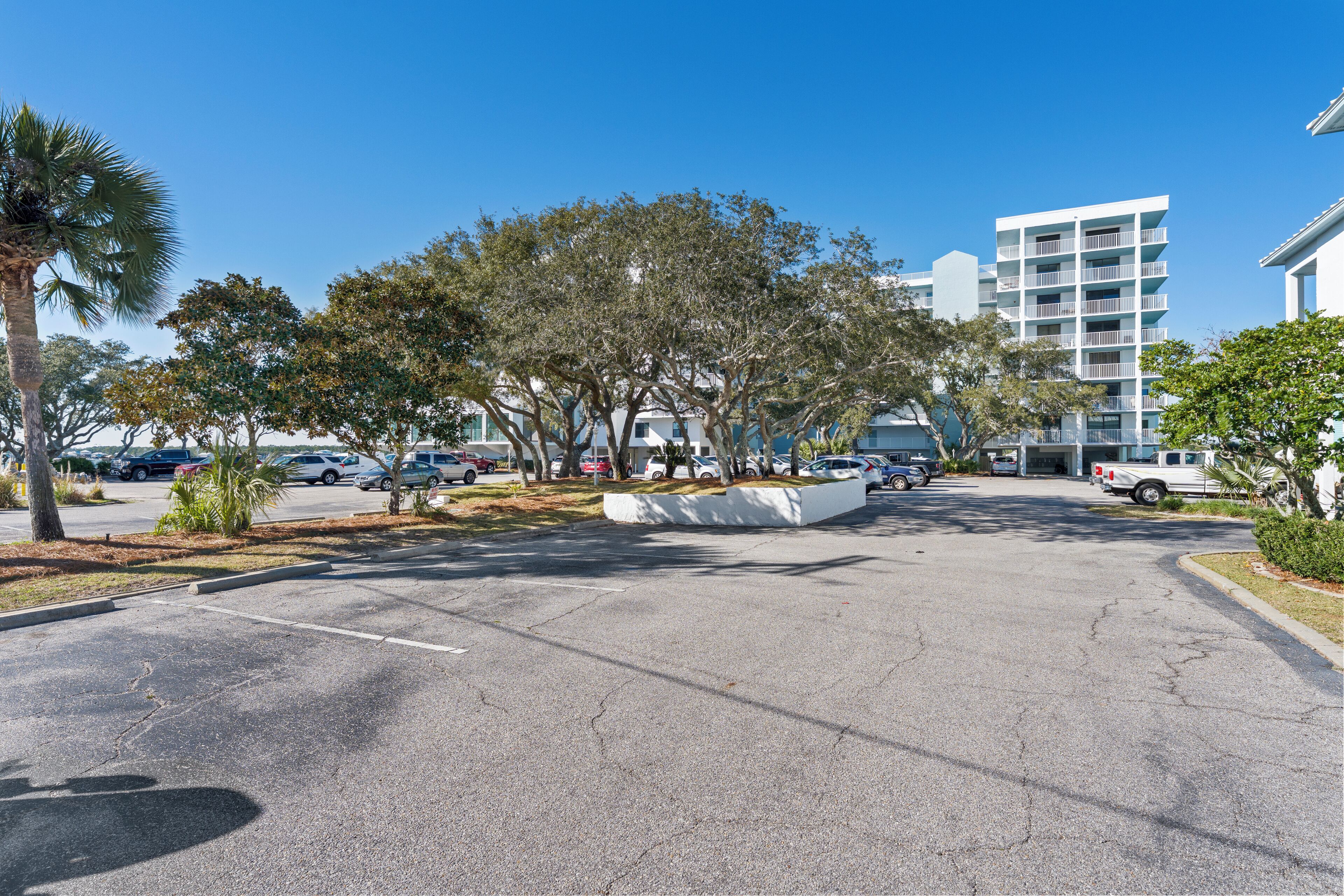 A parking lot with cars, a white building with balconies, and trees.