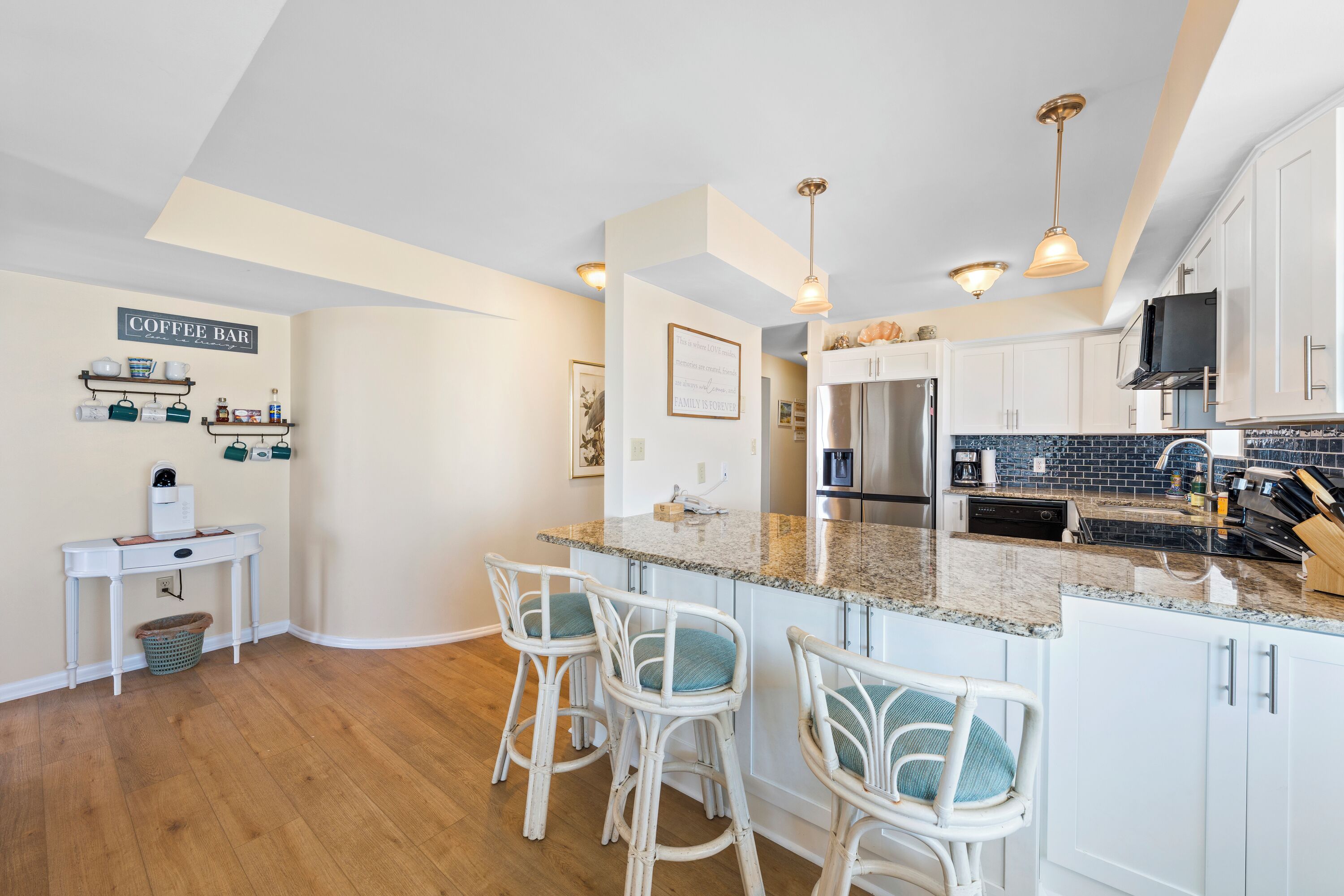 A modern kitchen with white cabinets, a granite countertop, and a coffee bar area.