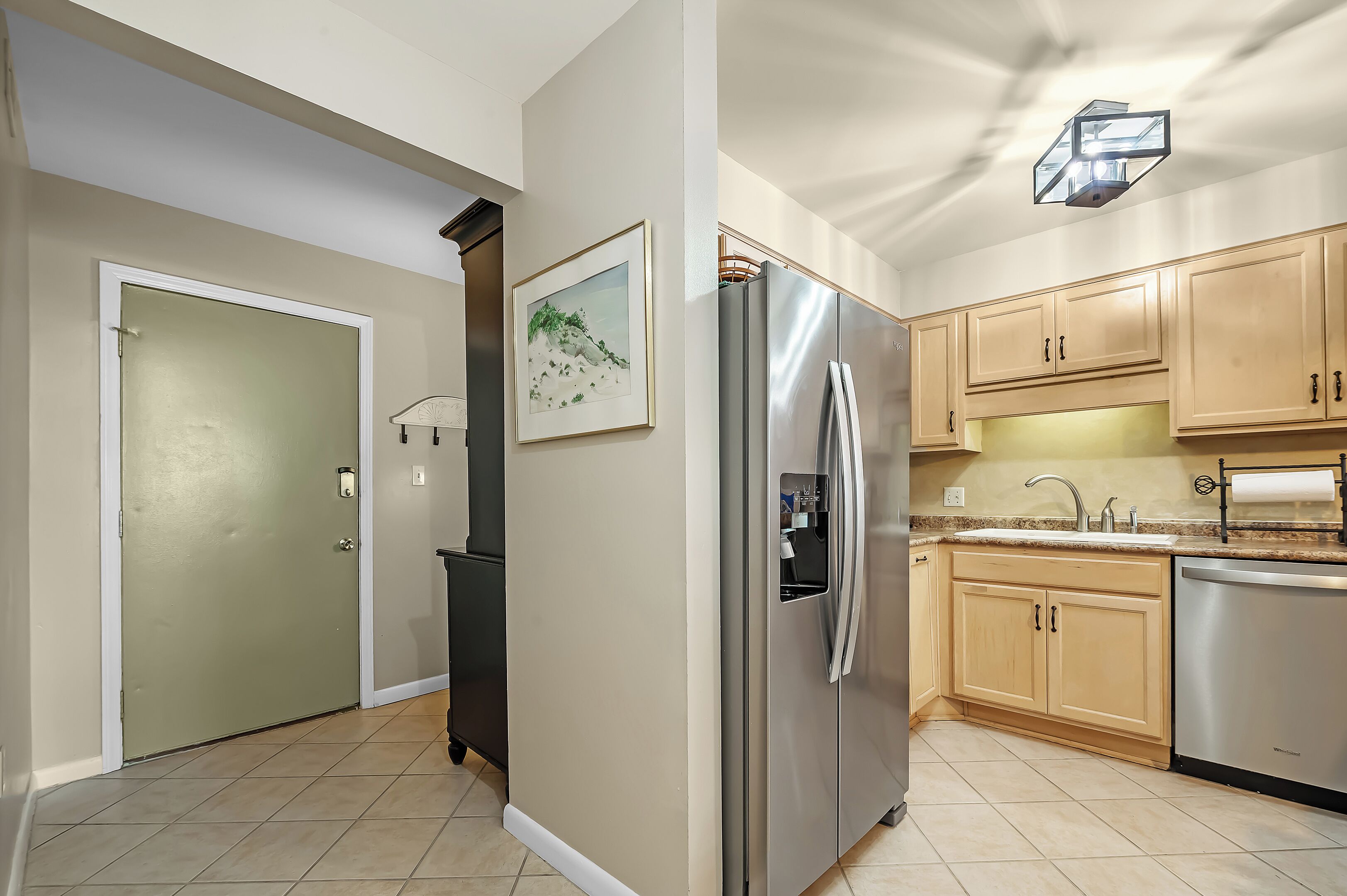 A modern kitchen with a stainless steel refrigerator, wooden cabinets, and a tiled floor.