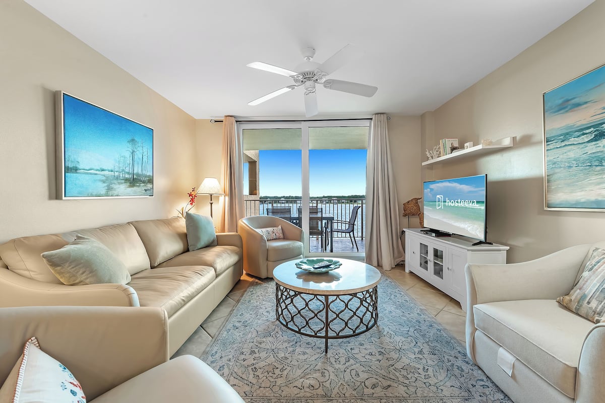 Un salon moderne avec un canapé beige, une table basse ronde, un téléviseur et un balcon offrant une vue dégagée.