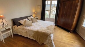 Un dormitorio con cama, mesitas de noche, armario y ventana con cortinas.