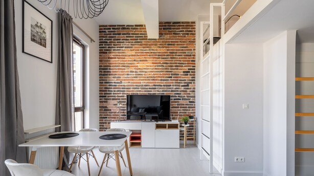 Un salon moderne avec un mur en briques, un téléviseur à écran plat, une table à manger avec des chaises et un meuble blanc.