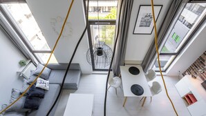 Un salon moderne avec un canapé gris, une table à manger et quatre chaises, et une vue sur l’extérieur grâce à de grandes fenêtres.