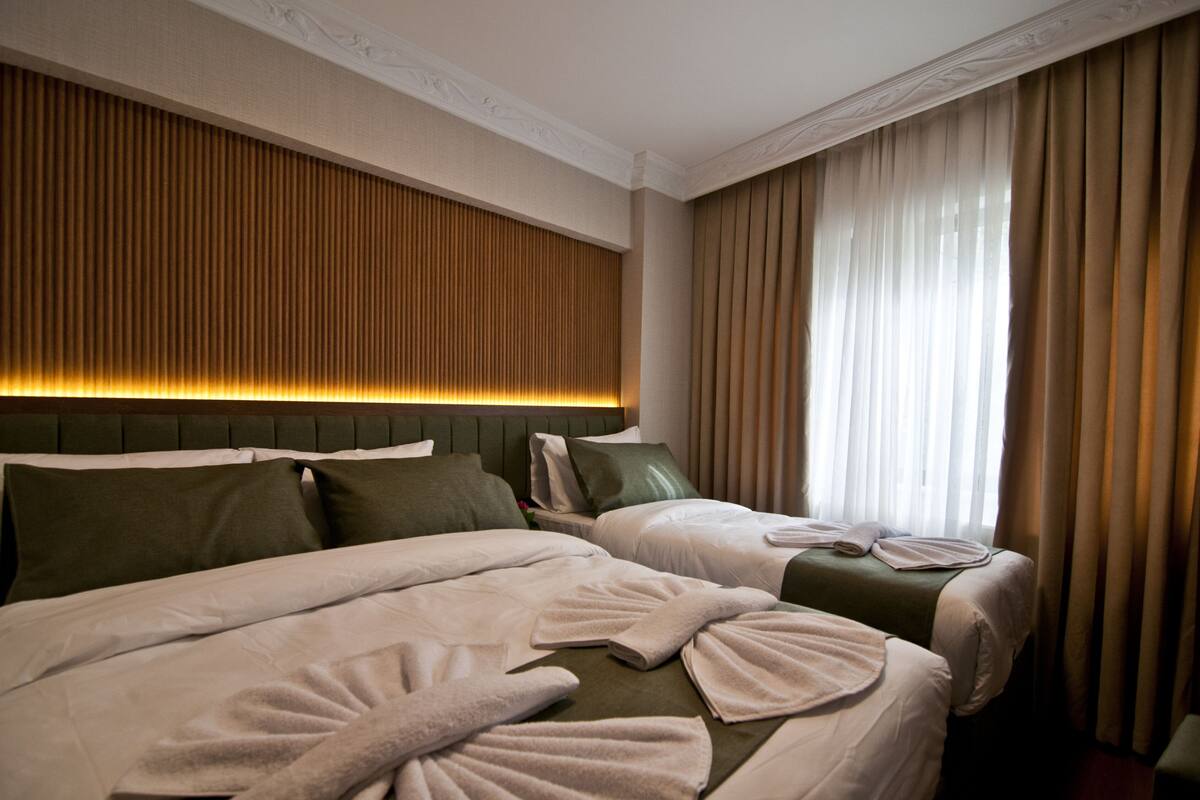 A hotel room with two beds, a headboard with vertical slats, and a large window with curtains.