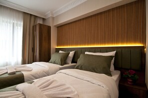 Una habitación de hotel con dos camas, cabecera de madera, mesita de noche con un florero y una ventana con cortinas.