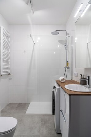 A modern bathroom with a shower, toilet, and a sink with a wooden countertop. - RentPlanet - Apartamenty Miedziana (Wroclaw)