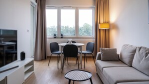 A modern living room with a sofa, a dining table with chairs, a TV, and a window with curtains. - RentPlanet - Apartamenty Miedziana (Wroclaw)