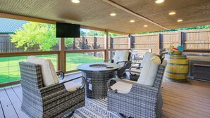 Un patio couvert aménagé avec des meubles en osier, une table ronde et un foyer.
