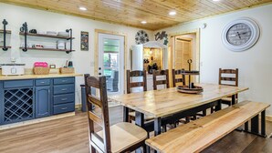 Une table à manger en bois, avec des bancs, entourée de chaises, dans une pièce dont le plafond et les murs sont recouverts de bois.