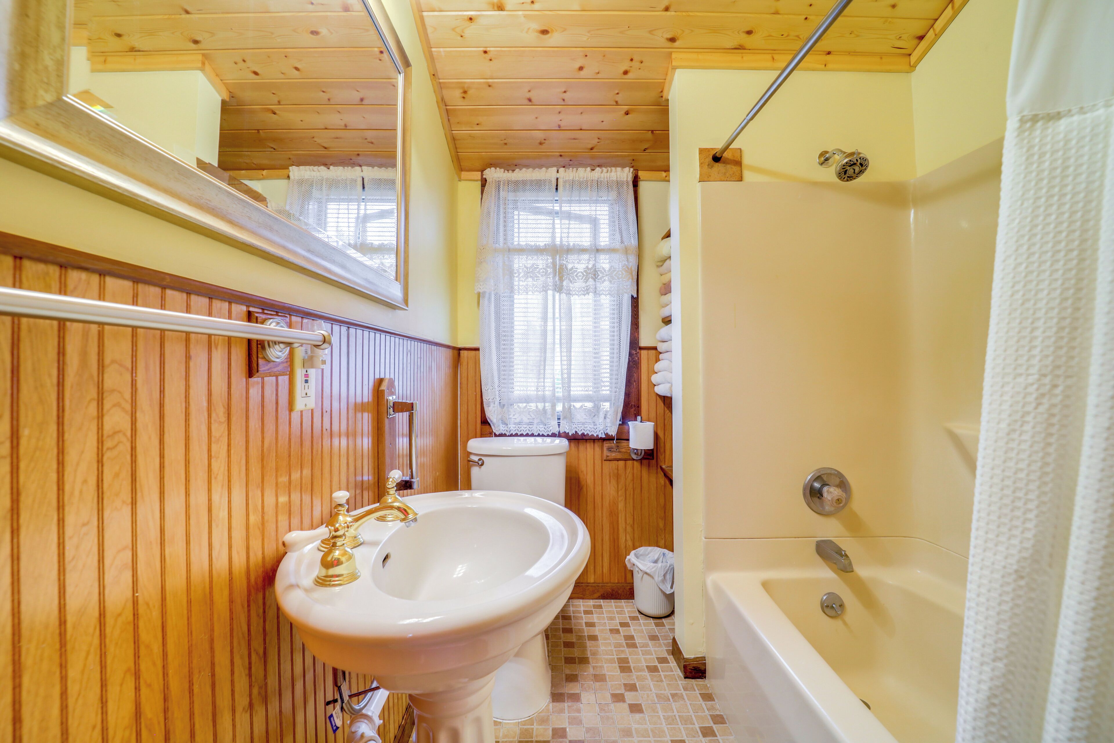 A bathroom with wooden paneling, a sink, toilet, and bathtub.