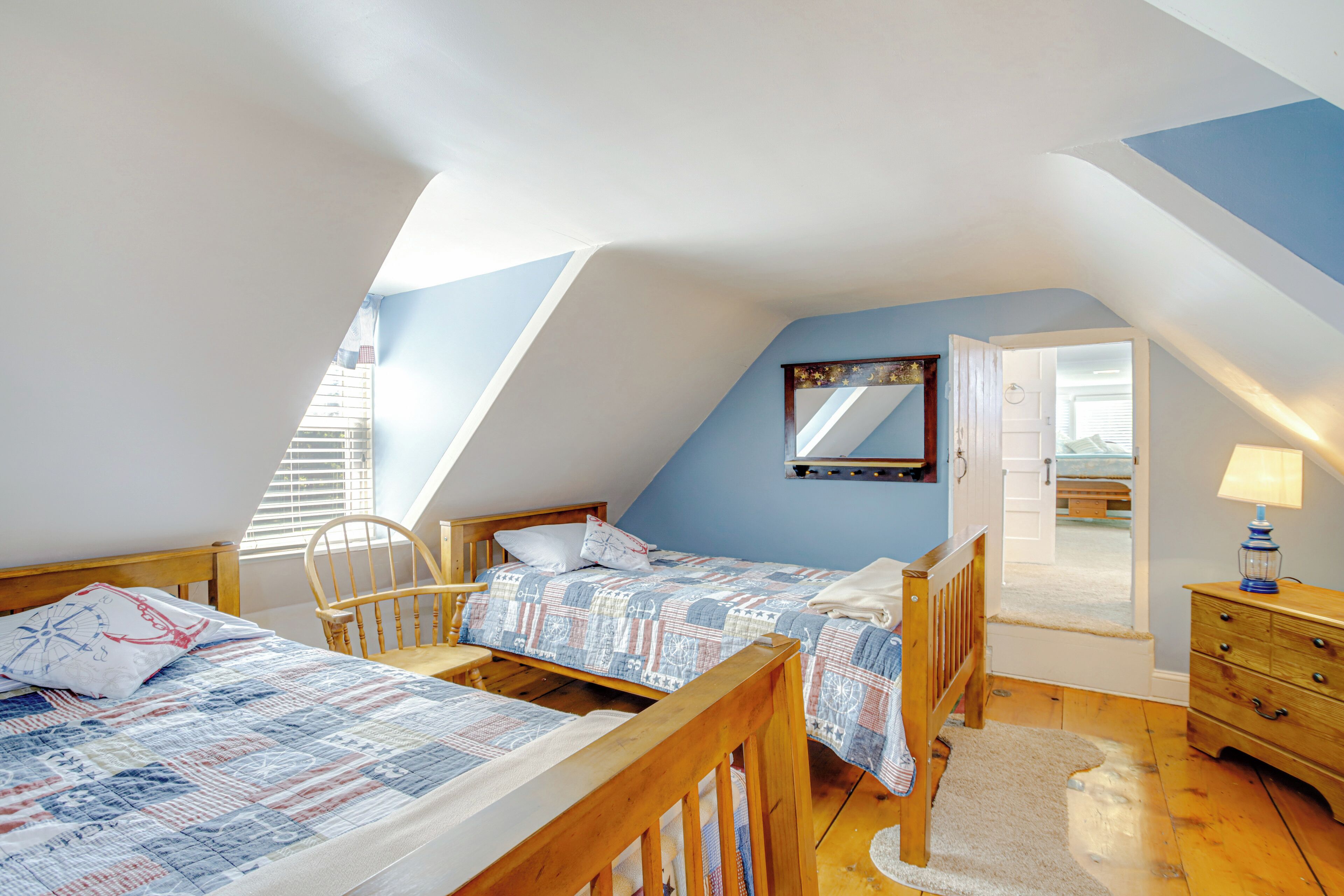 A bedroom with two beds, a wooden chair, a dresser, and a mirror on the wall.