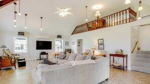A spacious living room with a large grey sofa, wooden flooring, a ceiling fan, and a staircase leading to an upper level. - Waterfront Cambridge Home: Pool & Dock! (Cambridge)
