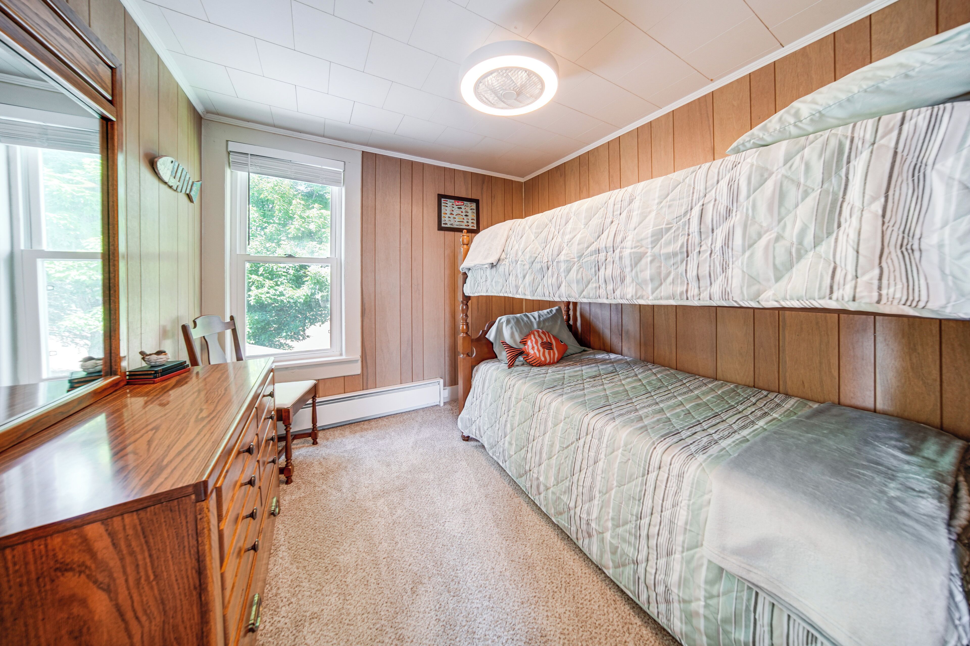 A bedroom with a bunk bed, a wooden dresser, a desk, and a window with a view of trees.