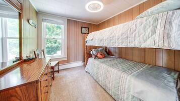 A bedroom with a bunk bed, a wooden dresser, a desk, and a window with a view of trees.