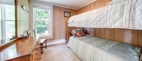 Een slaapkamer met een stapelbed, een houten dressoir, een bureau en een raam met uitzicht op bomen.
