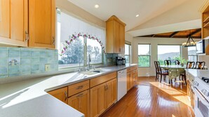A modern kitchen with wooden cabinets, a dishwasher, and a dining area with a table and chairs. - Kelseyville Home w/ Deck & Clear Lake Views! (Kelseyville)