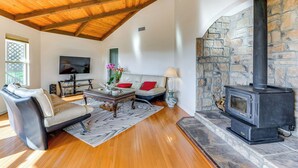 A living room with a stone fireplace, wooden ceiling beams, a sofa, and a television. - Kelseyville Home w/ Deck & Clear Lake Views! (Kelseyville)