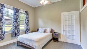 A bedroom with a bed, a nightstand, a dresser, a window with curtains, a door with a window, and a ceiling fan. - Jackson Family Home ~ 5 Mi to Downtown! (Jackson)