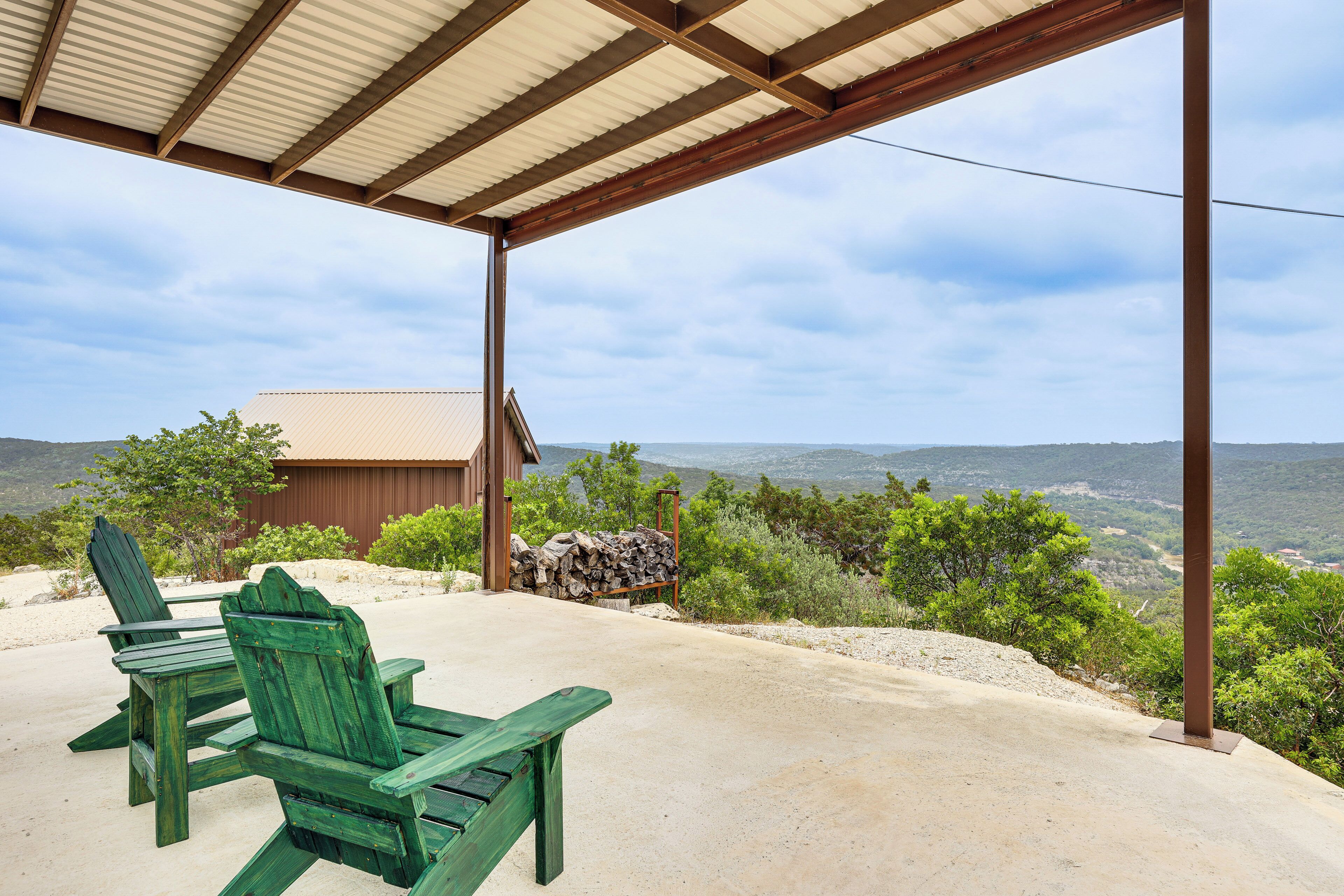 A covered outdoor seating area with Adirondack chairs, a wooden table, and a view of a mountainous landscape.