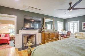 Une chambre à coucher avec une cheminée, un grand lit, une commode, un téléviseur et un ventilateur de plafond.