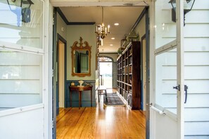 A hallway with wooden flooring, a chandelier, a mirror, a small table with decorative items, and a bookshelf. - Riverfront Denton Estate on 7 Acres w/ Heated Pool (Denton)