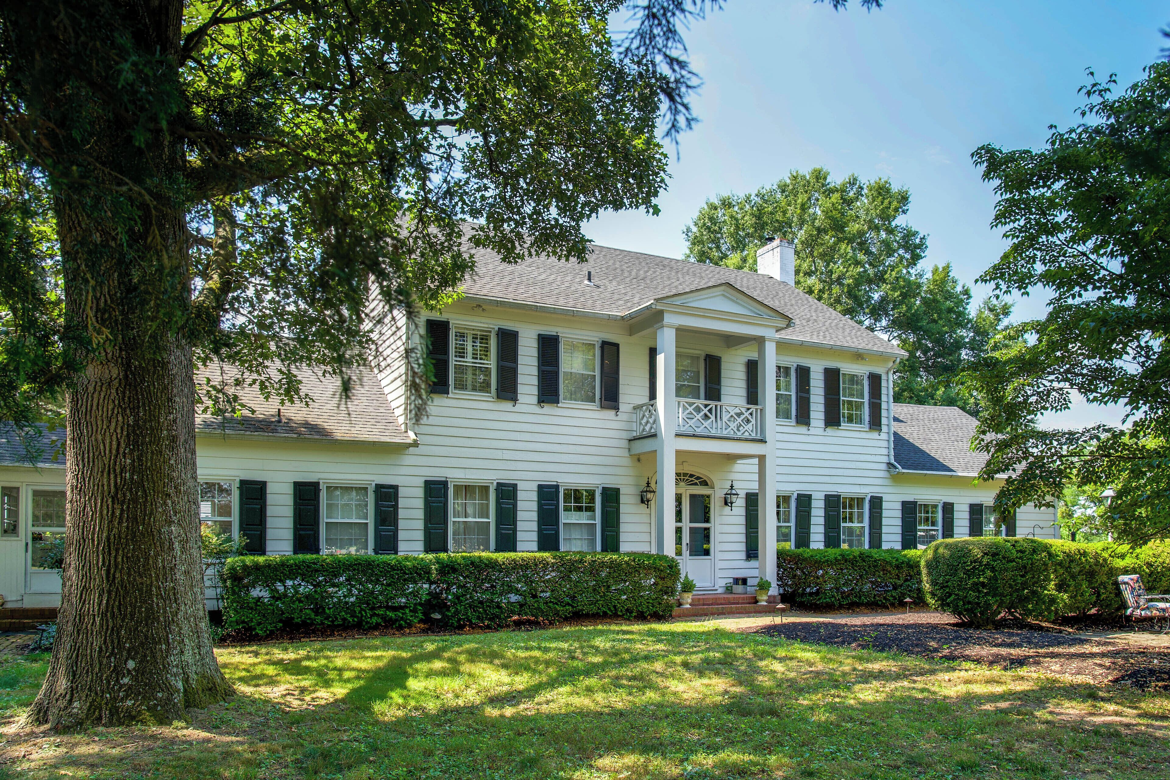 A two-story house with a front porch, a large tree, and well-maintained hedges.