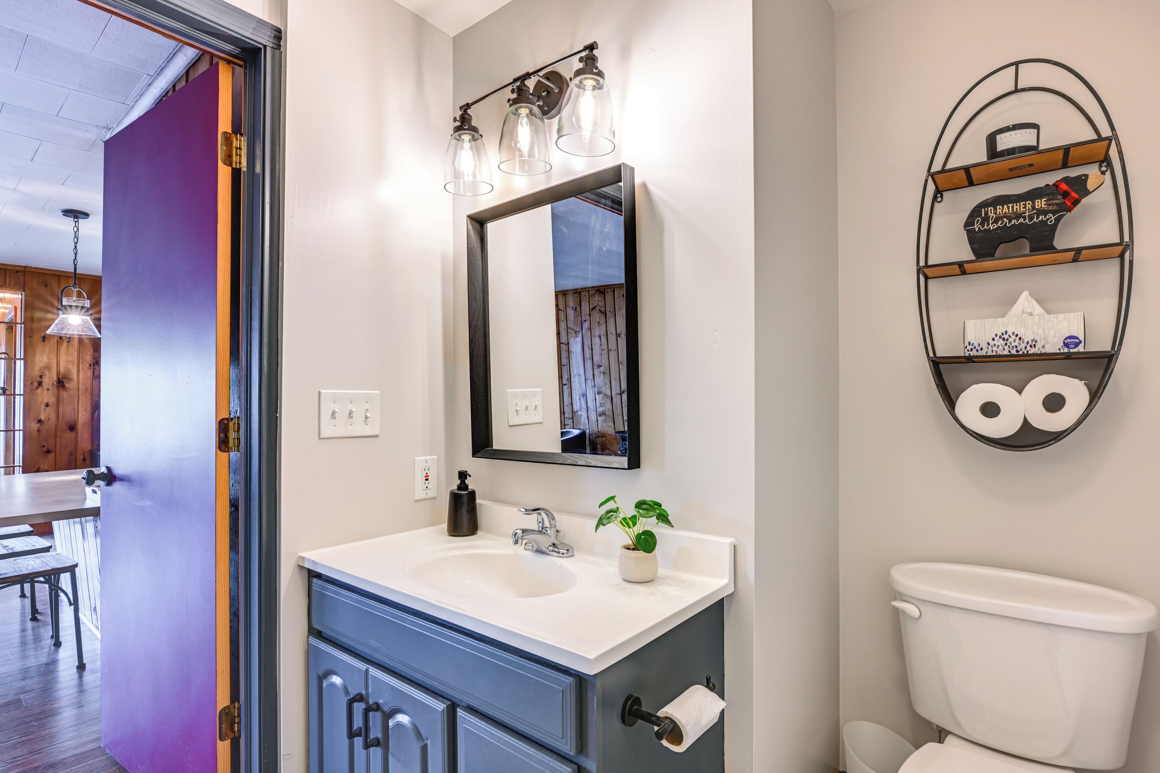 Une salle de bain avec un lavabo blanc, un miroir, des toilettes et une étagère décorée d’un ours.