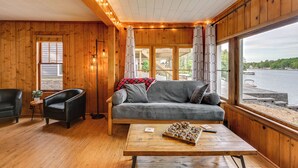 Interior acogedor de una cabaña con piso de madera, un sofá gris, un sillón negro y una mesa de centro de madera con pasteles.