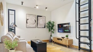 A modern living room with a sofa, coffee table, and a TV mounted on the wall displaying ESPN+ and Hulu logos. - Caddie St #A xxxxxxx (Austin)
