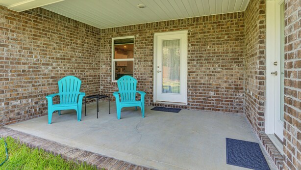 Een overdekt terras met twee turquoise Adirondack-stoelen, een bakstenen muur en een witte deur.