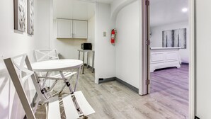 A room with a white dining table and chairs, a small kitchenette with a microwave, and a door leading to another room with a white cabinet and a painting. - Convenient Apt: 2 Mi to Sprain Ridge Park! (Yonkers)