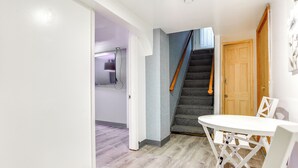 A hallway with a staircase, a wooden door, and a white table with chairs. - Convenient Apt: 2 Mi to Sprain Ridge Park! (Yonkers)