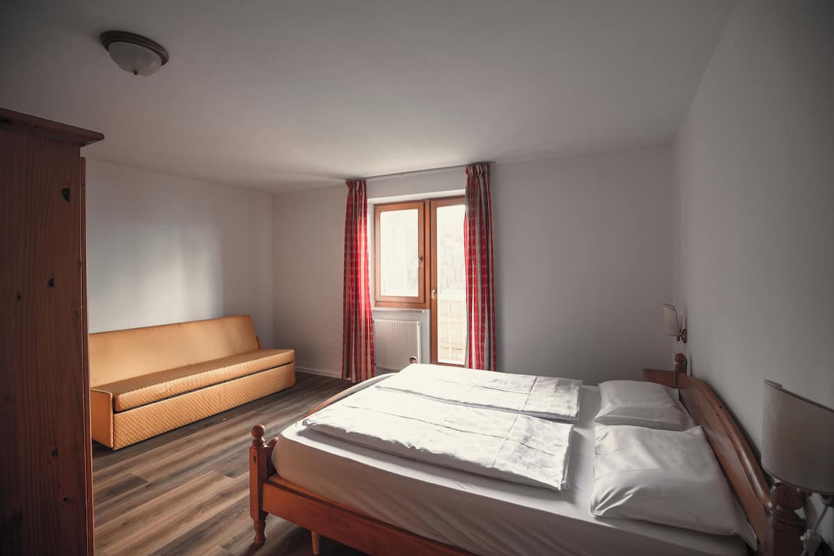 A bedroom with a wooden bed, a wooden bench, and a window with curtains.