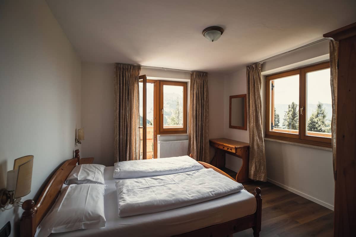 A bedroom with a wooden bed, a desk, and a window with curtains.