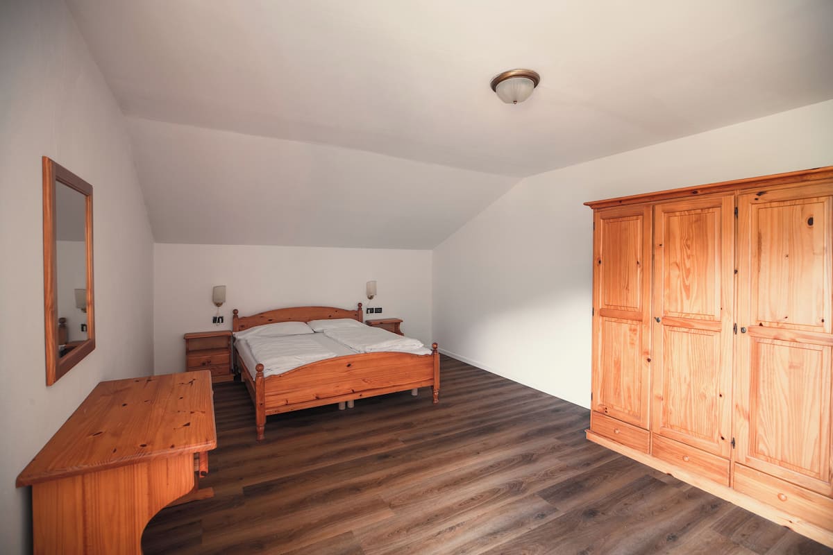A bedroom with a wooden bed, a wooden dresser, a wardrobe, and a mirror on the wall.