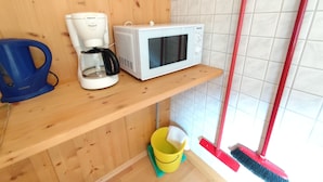Une petite cuisine équipée d’une machine à café, d’un four à micro-ondes et d’un balai appuyé contre le mur.