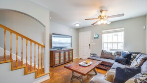 A living room with a wooden staircase, a television, a sofa, and a ceiling fan. - Steps to Beach & Pool Access: Port Aransas Condo (Port Aransas)