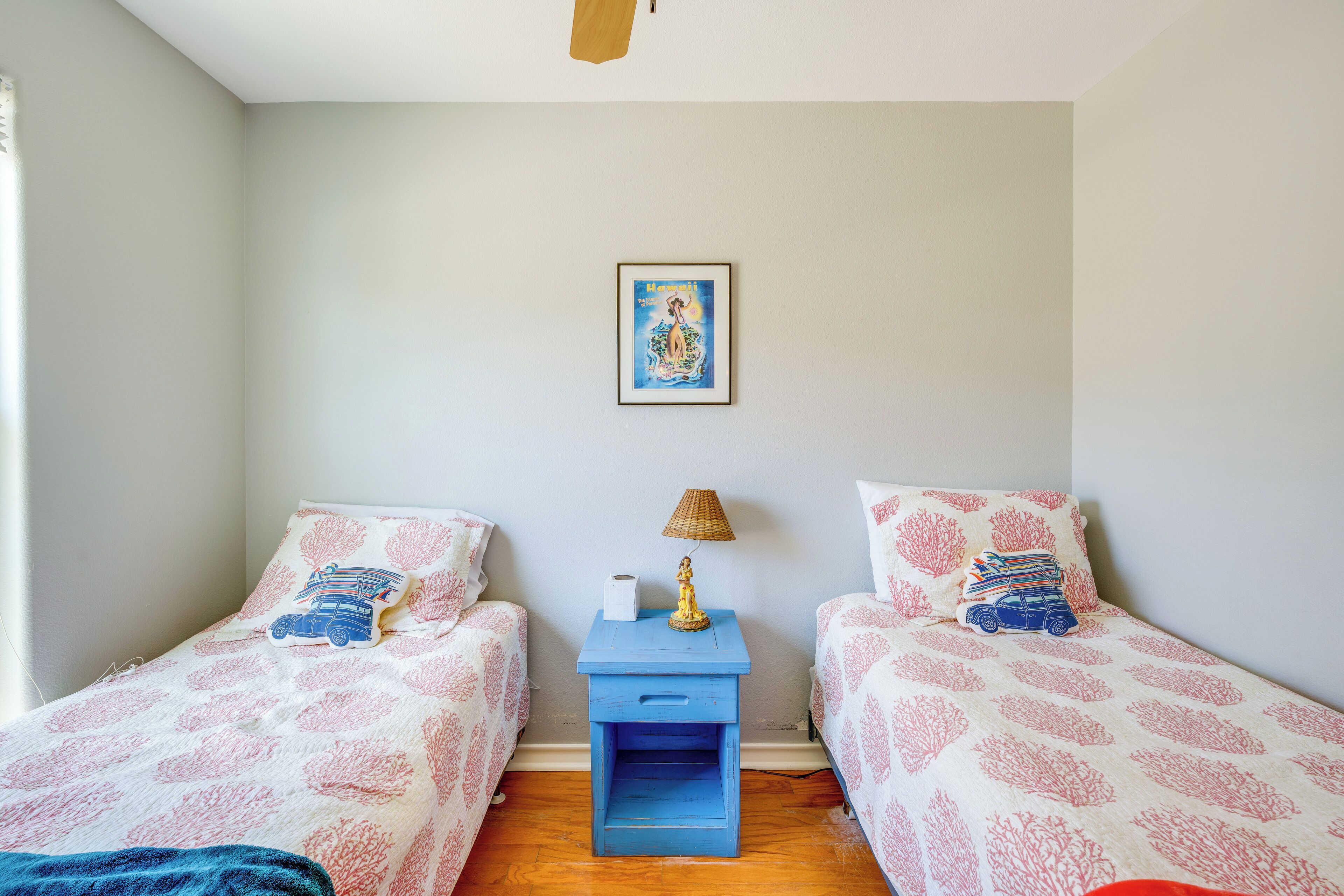A bedroom with two beds, each with a patterned bedspread, a small bedside table with a lamp, and a framed picture on the wall.