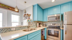 A kitchen with teal cabinets, stainless steel appliances, a tiled backsplash, and pendant lighting. - Steps to Beach & Pool Access: Port Aransas Condo (Port Aransas)