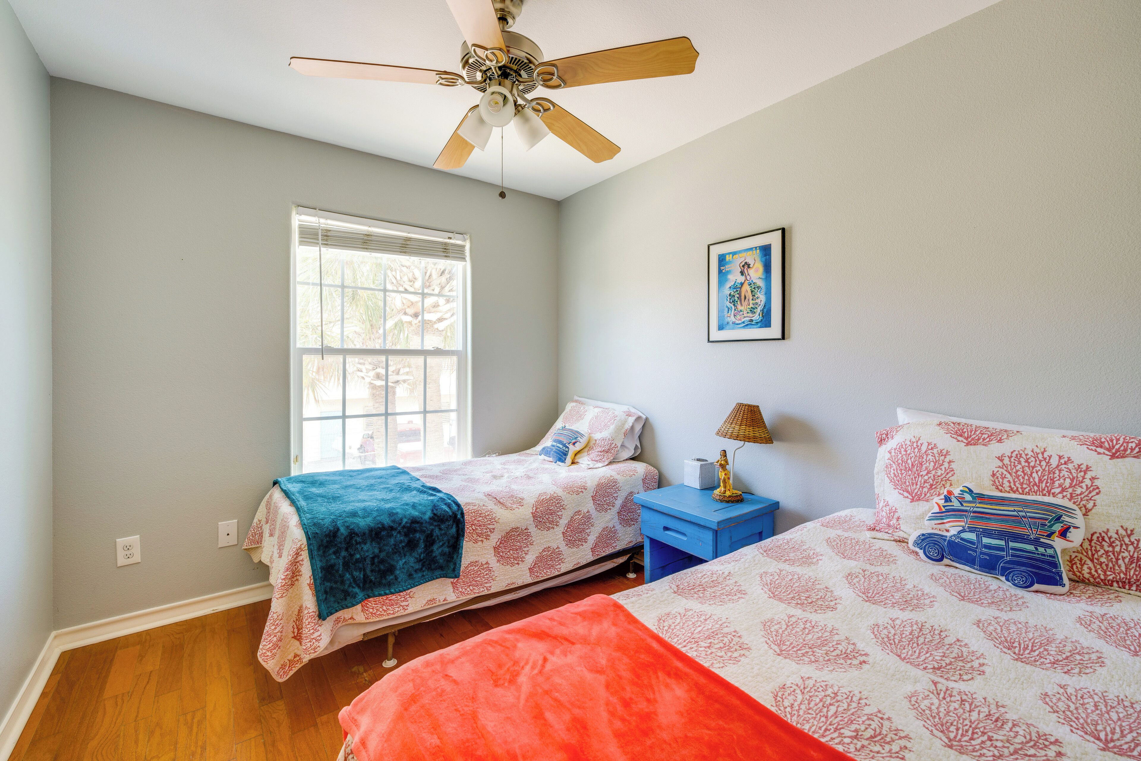 Une chambre avec deux lits, un ventilateur de plafond, une fenêtre et une table de chevet avec une lampe.
