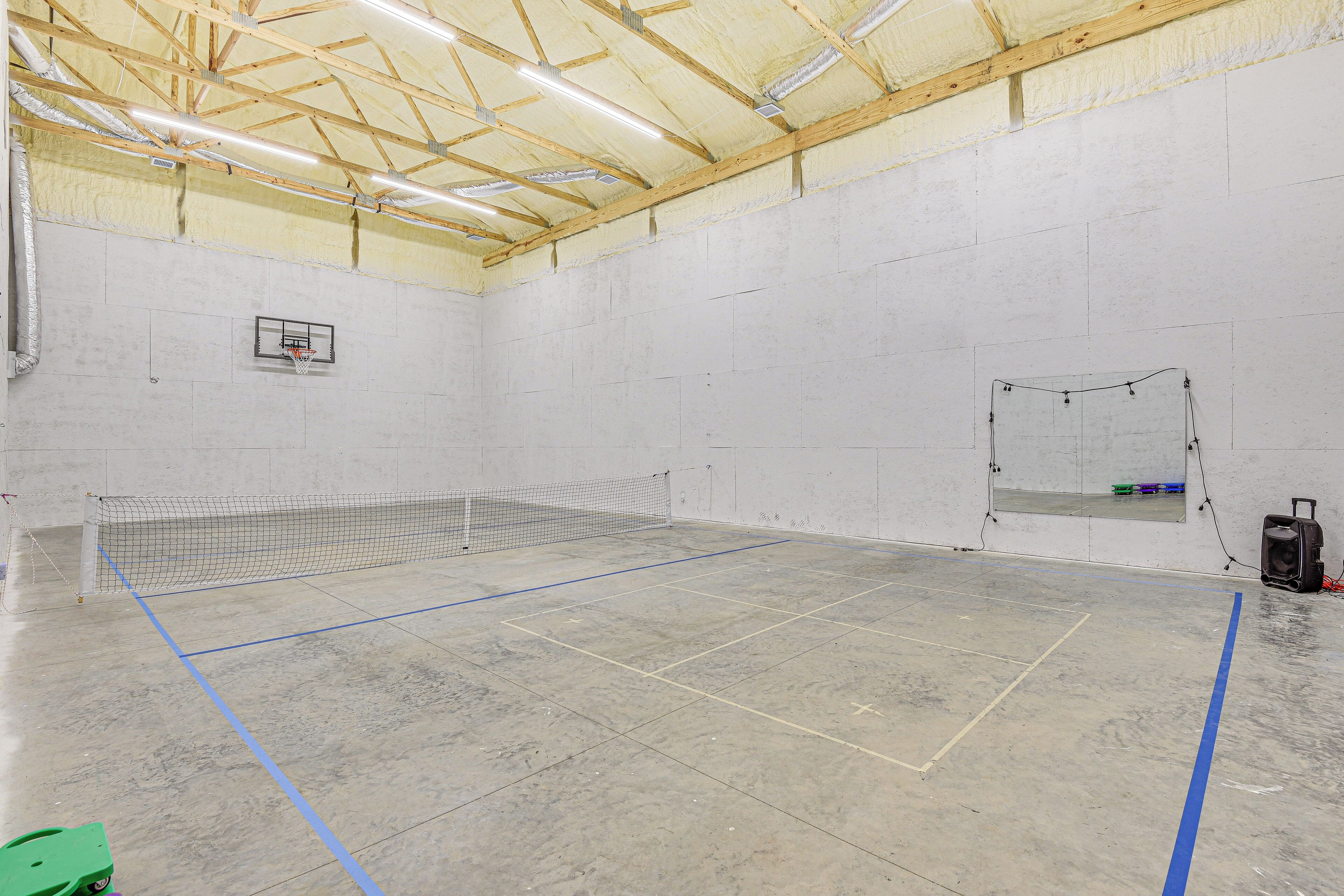 A spacious indoor tennis court with a wooden ceiling, a basketball hoop, and a net.