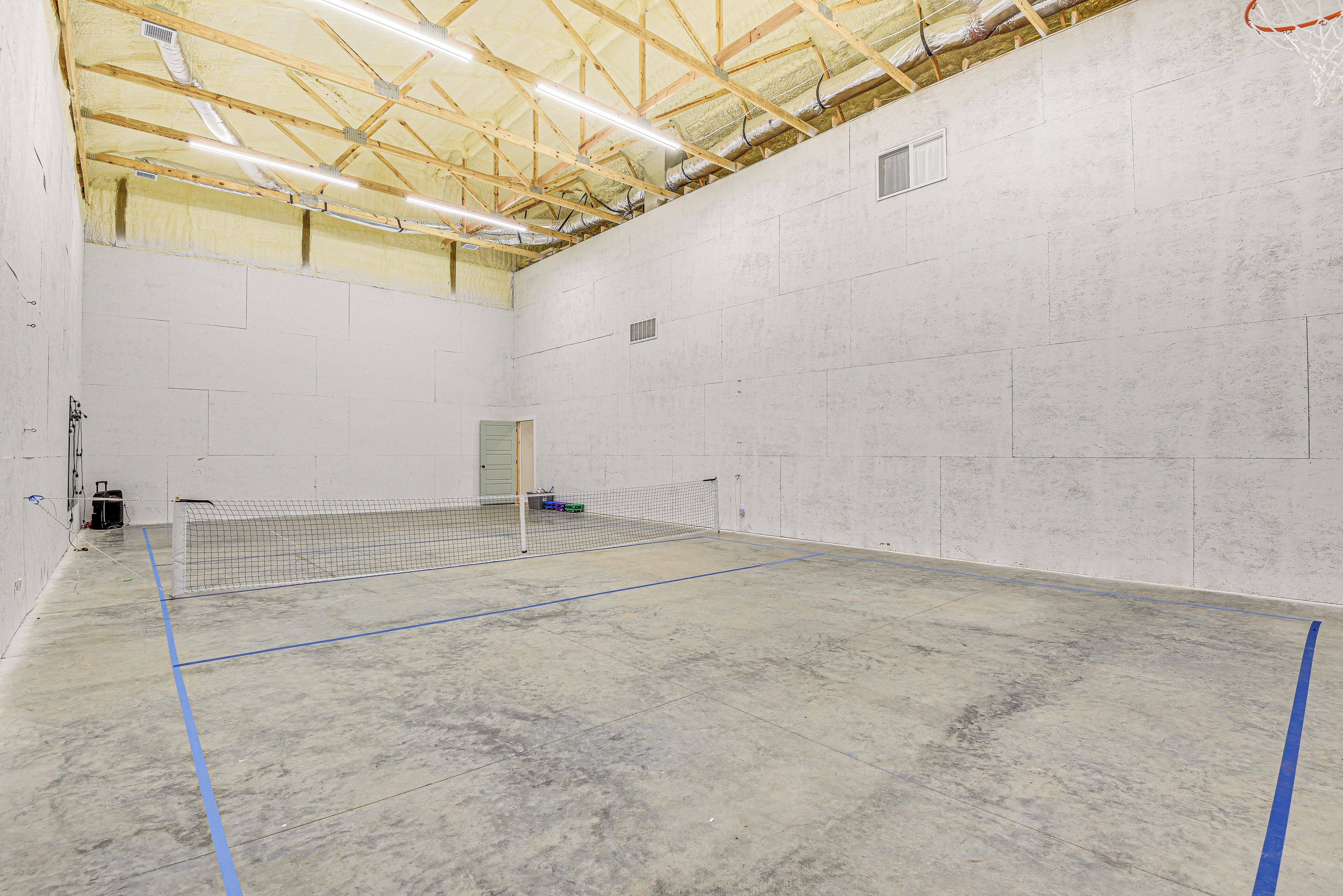 An indoor sports facility with a tennis court, visible ceiling structure, and a door.