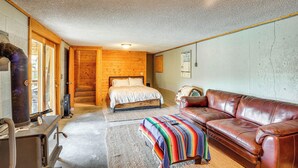 A cozy room with a bed, a leather sofa, a fireplace, and a wooden wall. - Dubois Riverfront Lodge w/ On-site Fishing & Views (Dubois)