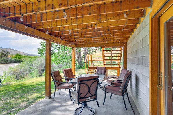 Un patio al aire libre con vigas de madera, una mesa de vidrio y varias sillas acolchadas.