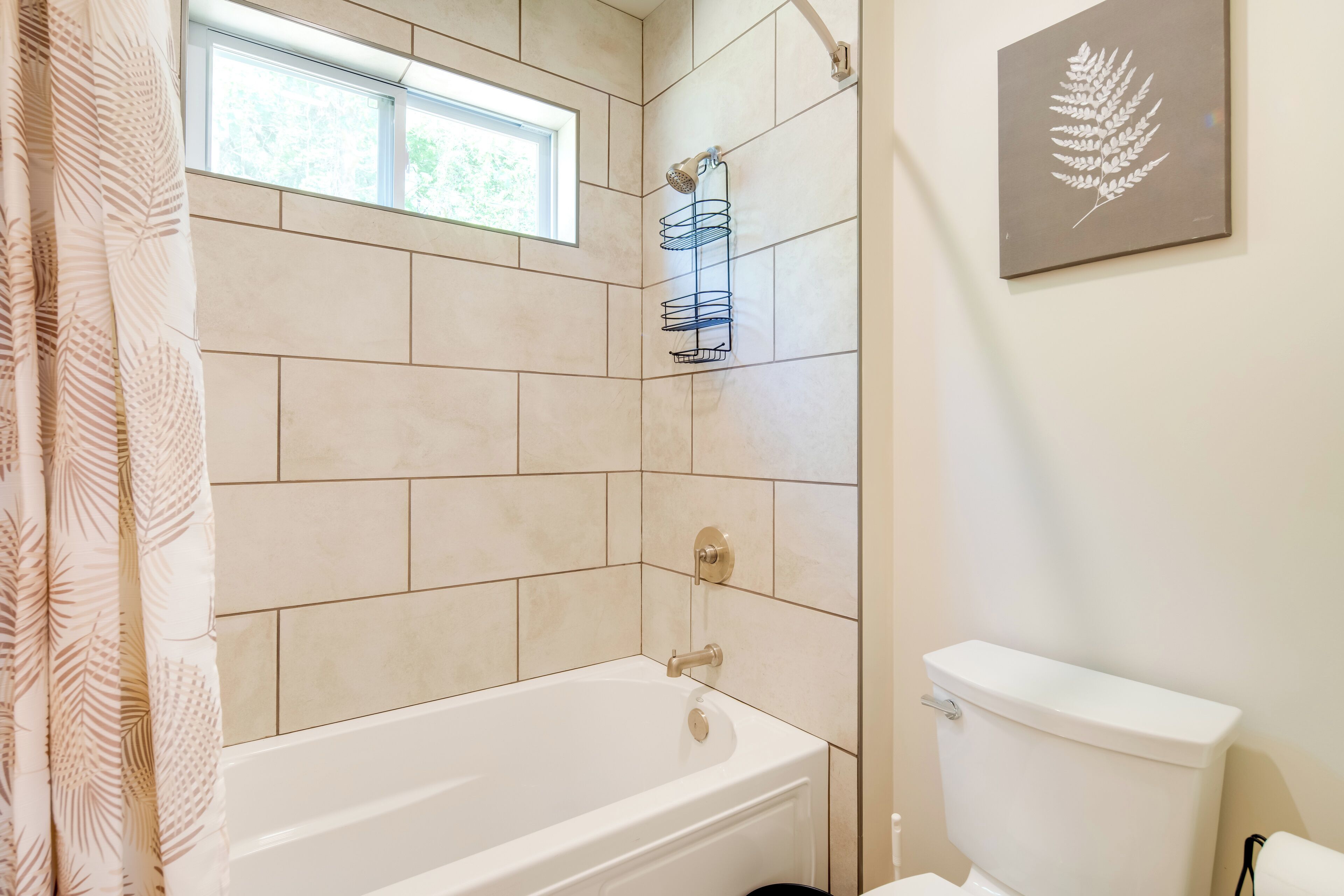 Une salle de bain avec une baignoire, des toilettes, une fenêtre et une étagère fixée au mur.